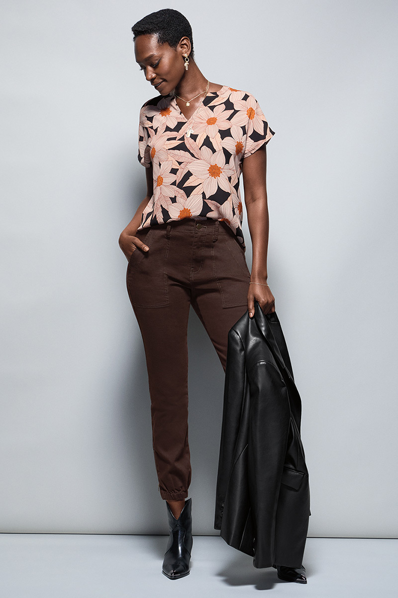 Model Wearing Meadow Top in Daisy Print, James Jacket in Black, Compass Pant in Dark Chocolate, Dream Weaver Necklace in Gold, Dream Earrings in Gold.