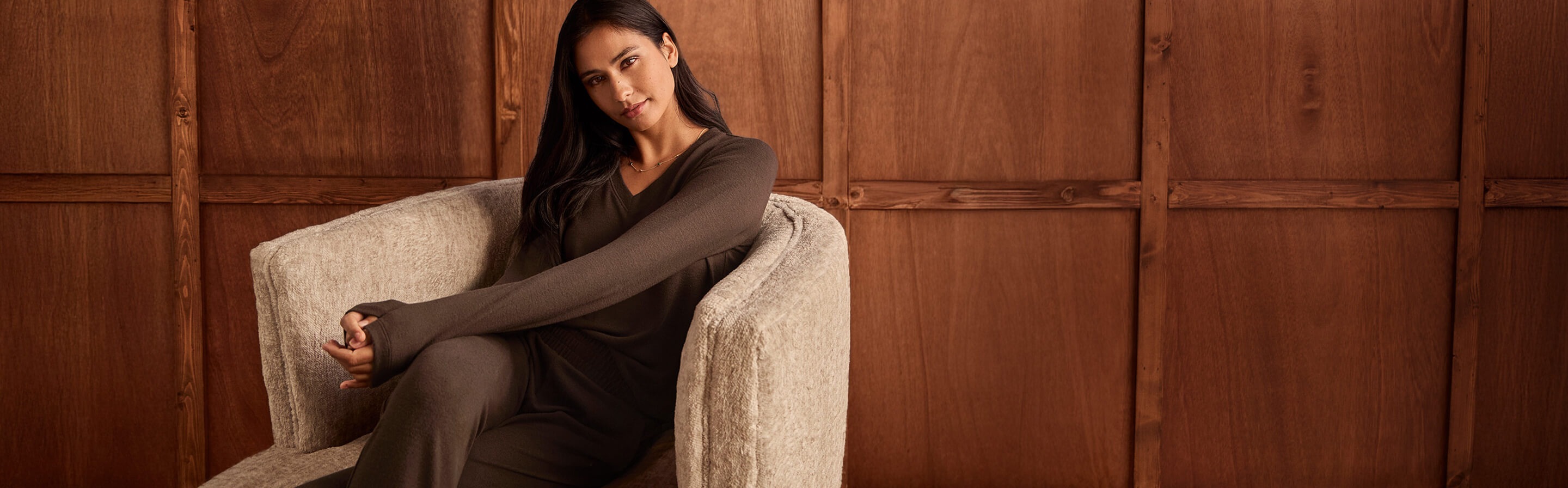 a model who is sitting in a club chair in a wood paneled room, wearing items from the new cabi Fall 2025 Collection