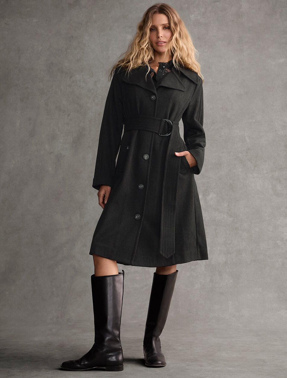 A female model wearing a long black coat with black leather boots